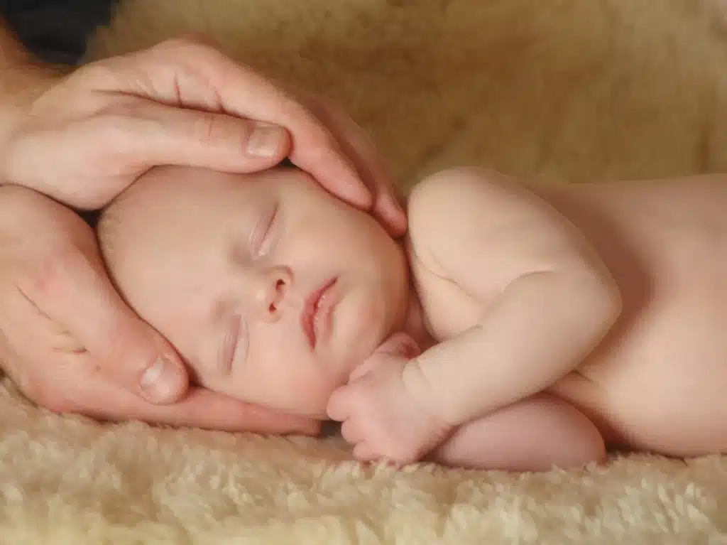 Hände halten behutsam den Kopf eines schlafenden Babys.