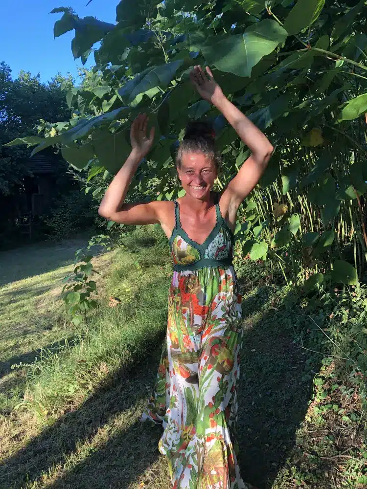 Alma tanzt barfuß im Garten, die Arme über dem Kopf.