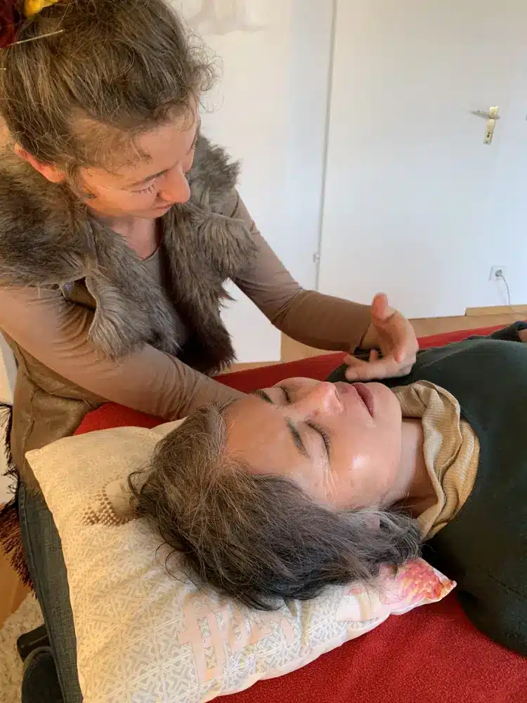 Alma behandelt eine Patientin am Kopf, beide wirken ganz in Ruhe.